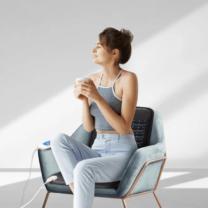 Woman seated on chair using Grooni PEMF Chair Mat Review setup for grounding and PEMF