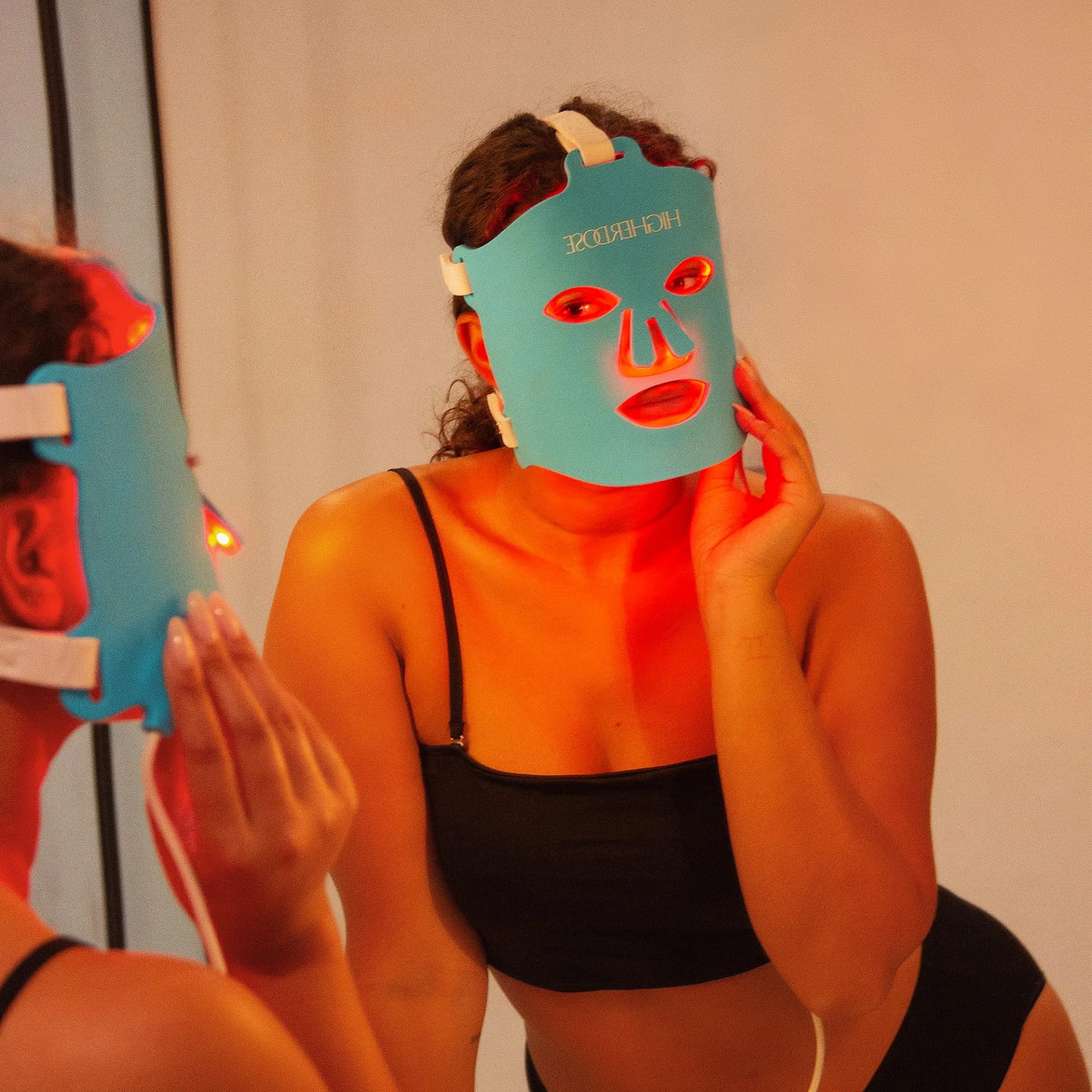 Donna che applica Maschera HigherDose per Terapia a Luce Rossa davanti allo specchio durante routine skincare