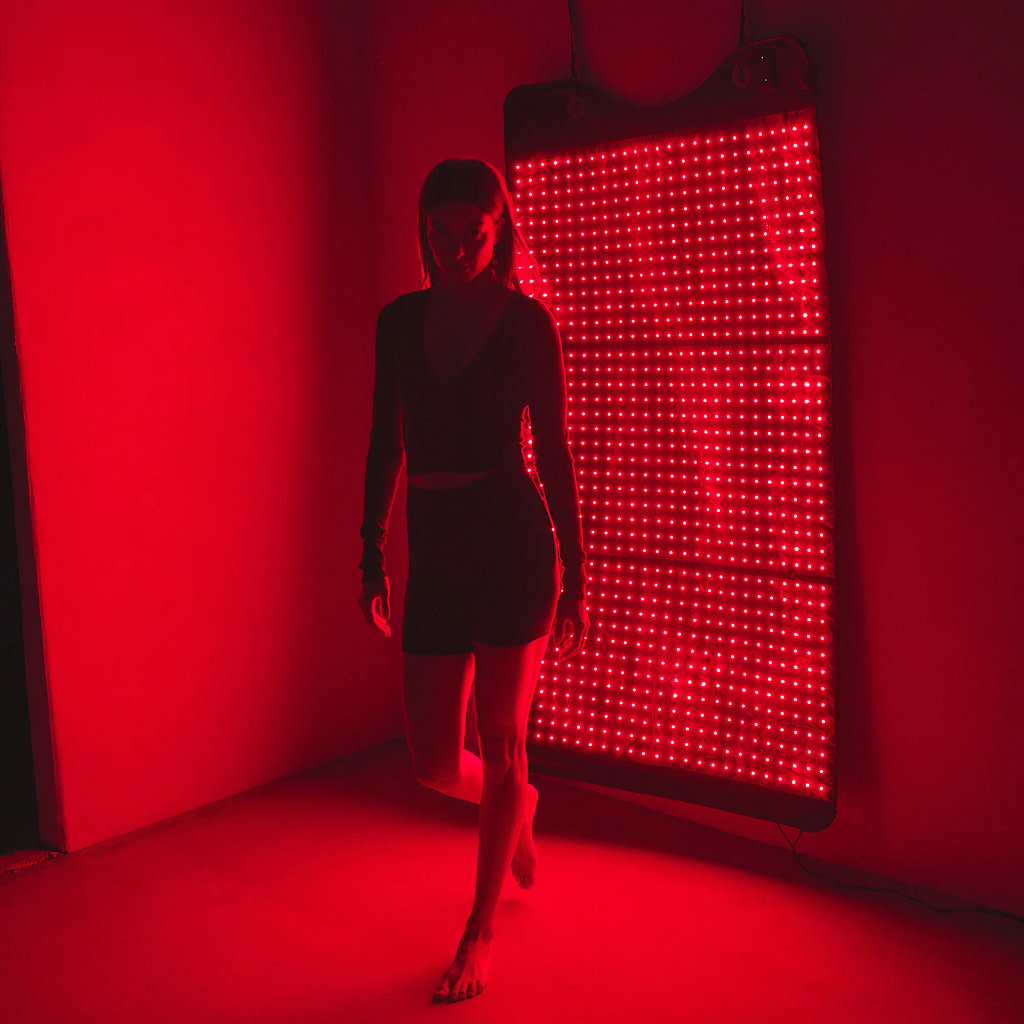 Woman using HigherDose Mat mounted on wall as standing LED therapy panel for vertical treatment