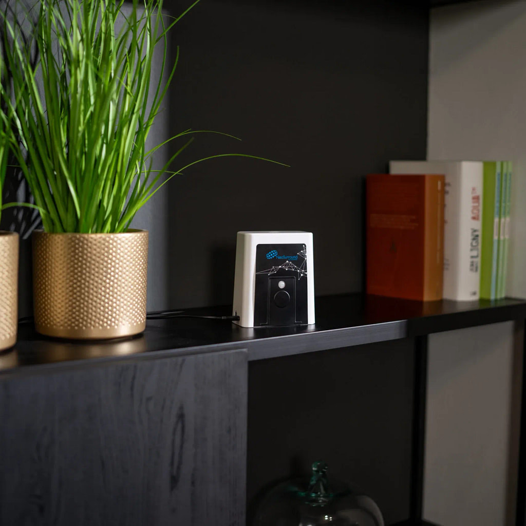 NeoSurround PEMF therapy device on a shelf between a plant and some books