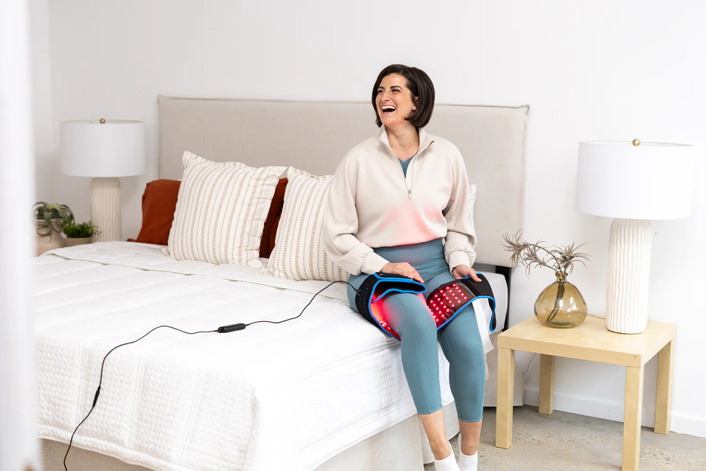 Woman relaxing with LifePro Red Light Belt wrapped around leg for evening pain relief routine