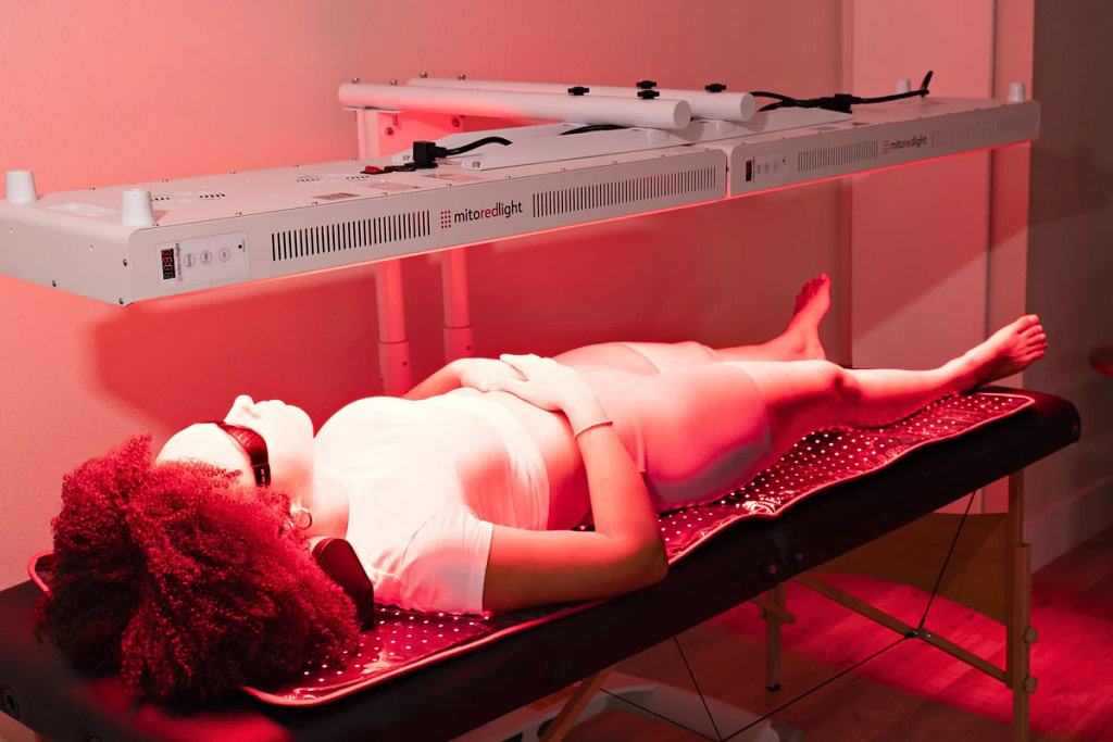 Woman lying on a treatment bed under a Mito Adapt red light panel mounted horizontally on its stand in a clinic