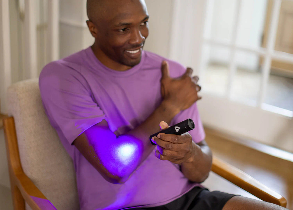 Man applying LifePro Lumicure to elbow joint in purple light mode for inflammation and recovery treatment