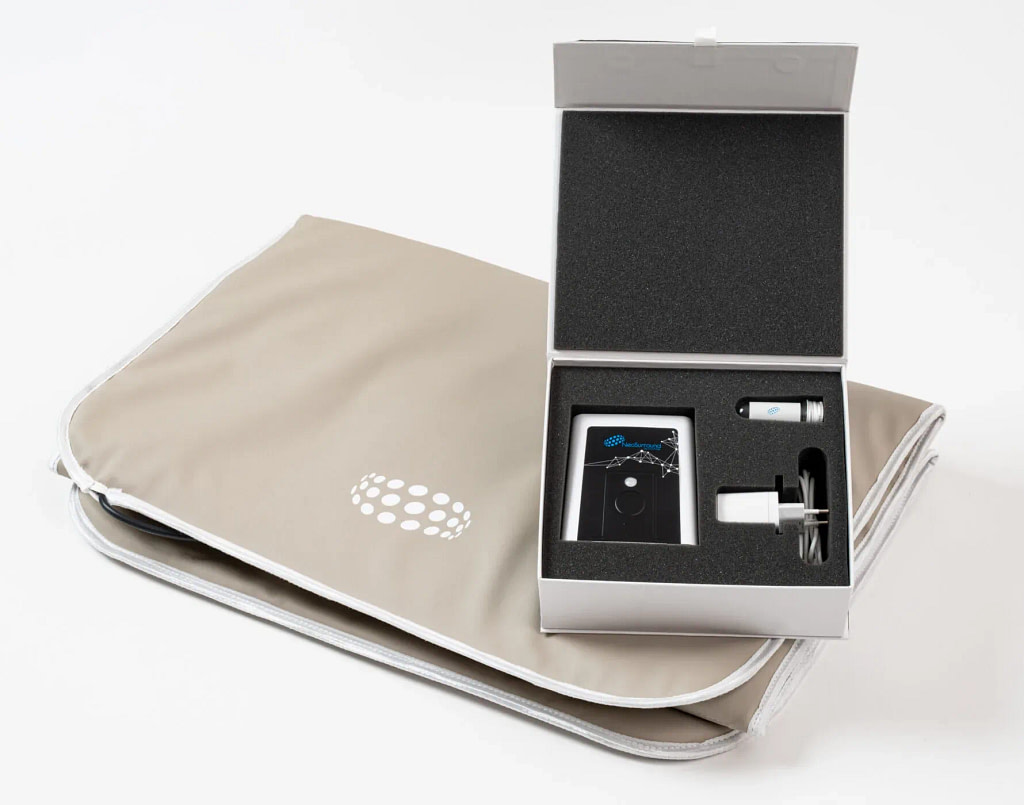 Open NeoSurround mat PEMF system box showing the room device, test tube, and charger