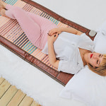 Woman relaxing on the Phymat Gemstones mat placed on a bed