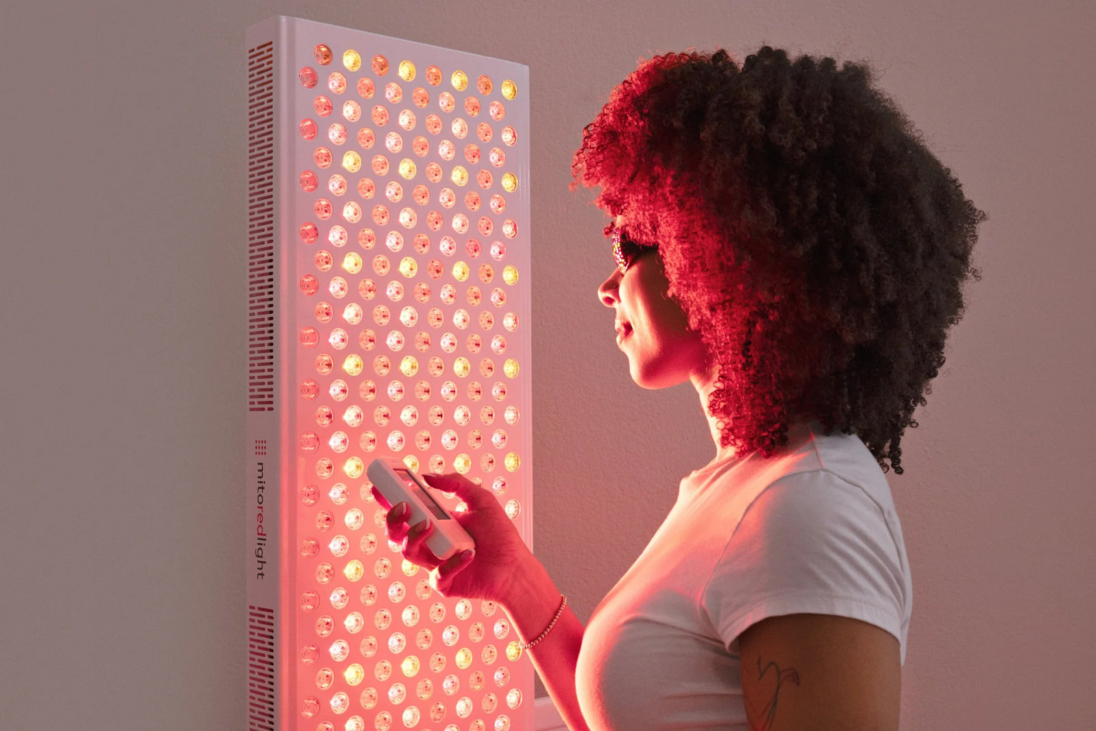 Woman using the MitoADAPT 4.0 app on her phone during a red light therapy session in front of the mito red light panel
