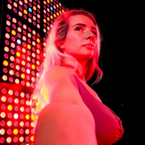User next to high intensity red light therapy panel for recovery