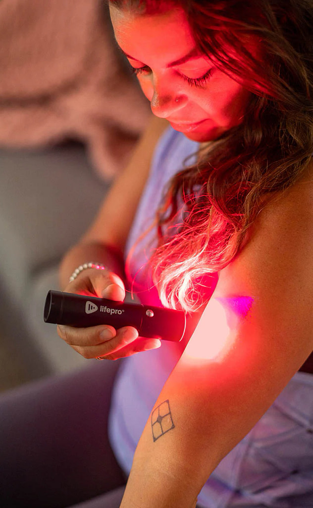 Woman applying LifePro Lumicure Torch to arm in red light mode for muscle recovery and skin rejuvenation