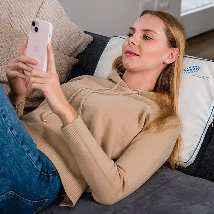 Woman using OmniPEMF NeoRhythm Pad on bed for relaxation