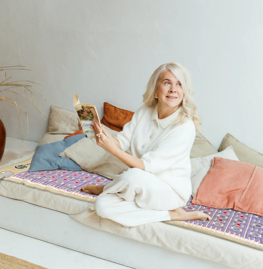 Senior woman reading a book while comfortably seated on HealthyLine TAJ PEMF Mat