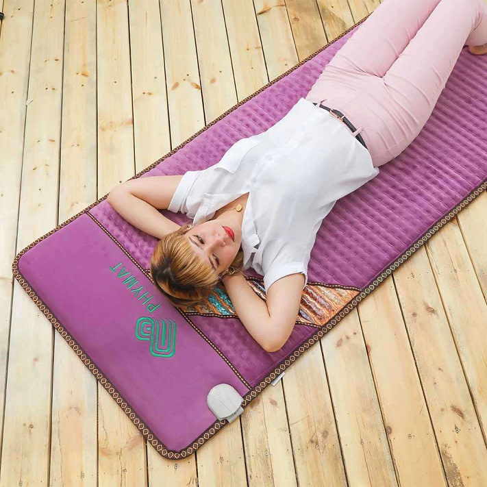 Woman lying relaxed on Phymat Amethyst PEMF Mat for full body PEMF and infrared therapy