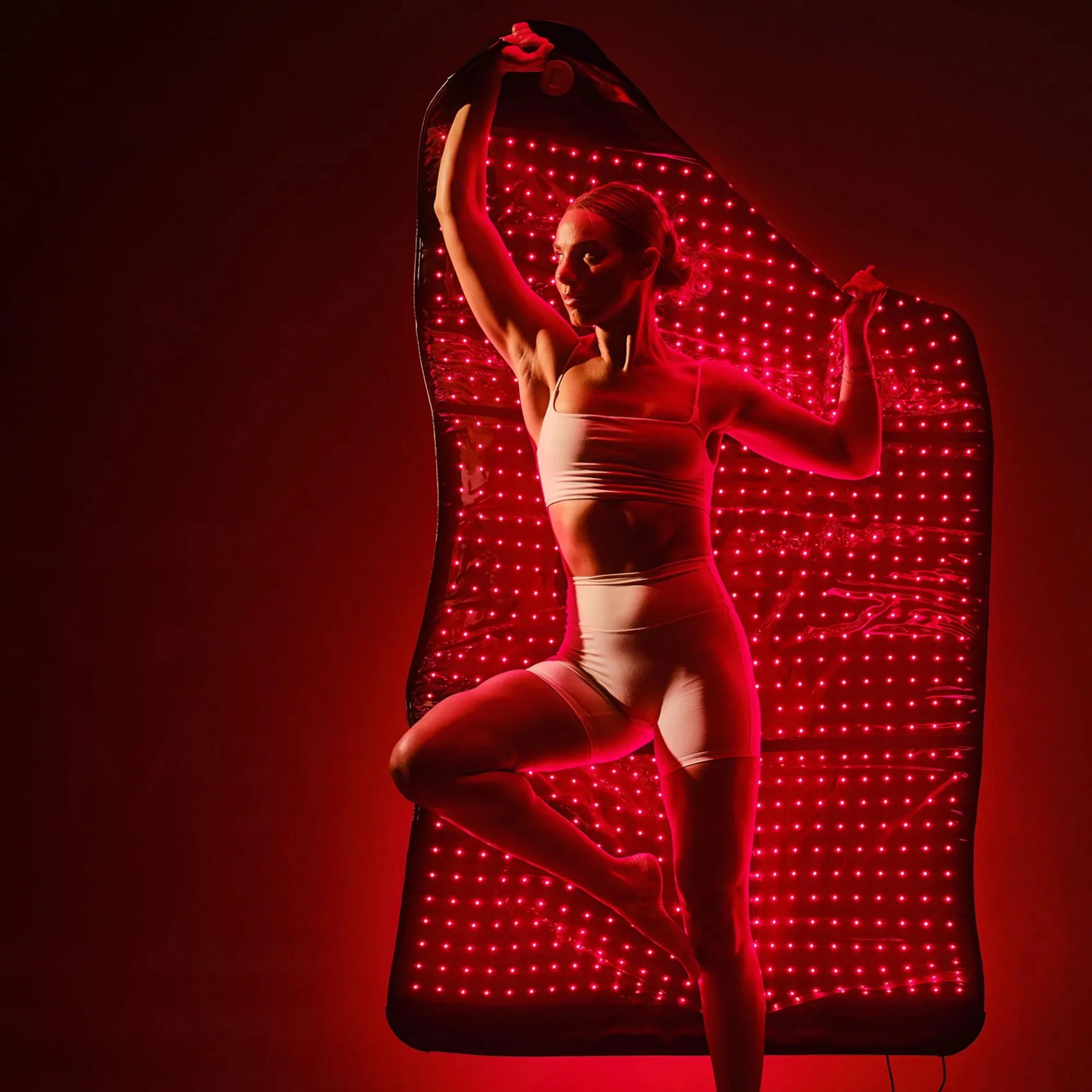 Woman wrapping HigherDose LED Mat around body demonstrating flexible blanket mode for 360-degree therapy