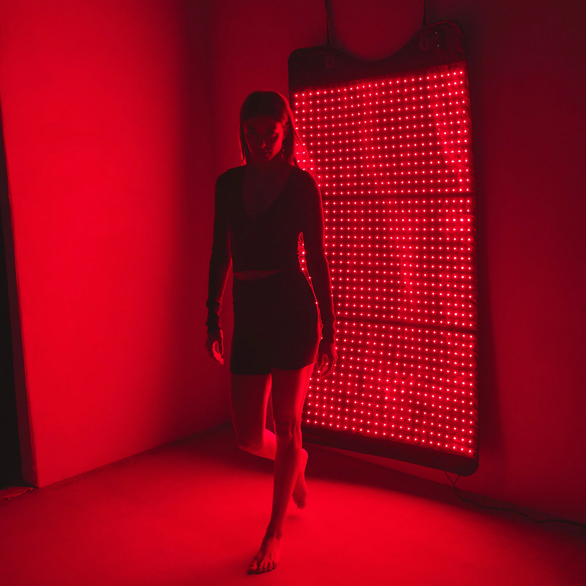 Woman using HigherDose Mat mounted on wall as standing LED therapy panel for vertical treatment