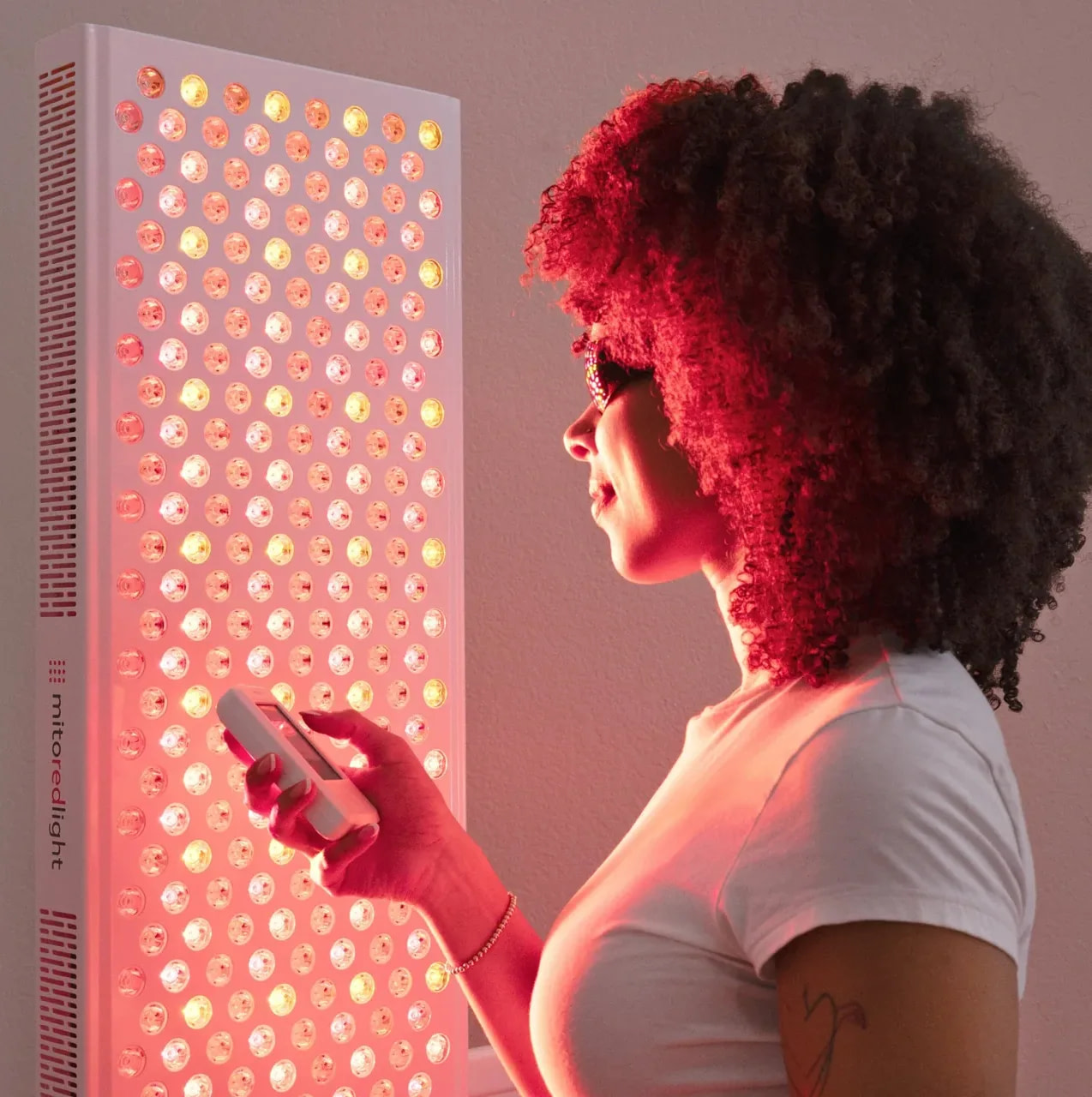 Woman using the MitoADAPT 4.0 app on her phone during a red light therapy session in front of the mito red light panel