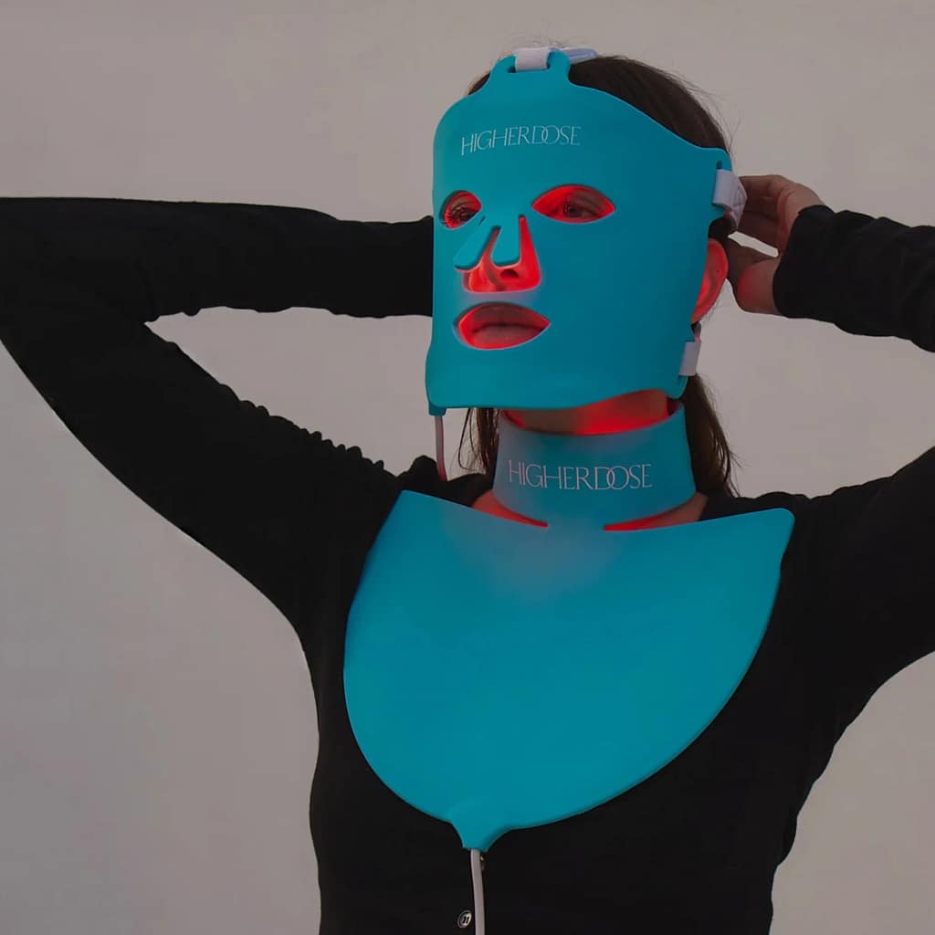 Woman using HigherDose Red Light Therapy Neck Enhancer simultaneously with face mask for comprehensive anti-aging system