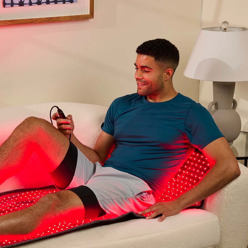 Man adjusting LifePro LED Mat intensity settings on sofa during comfortable red light therapy session