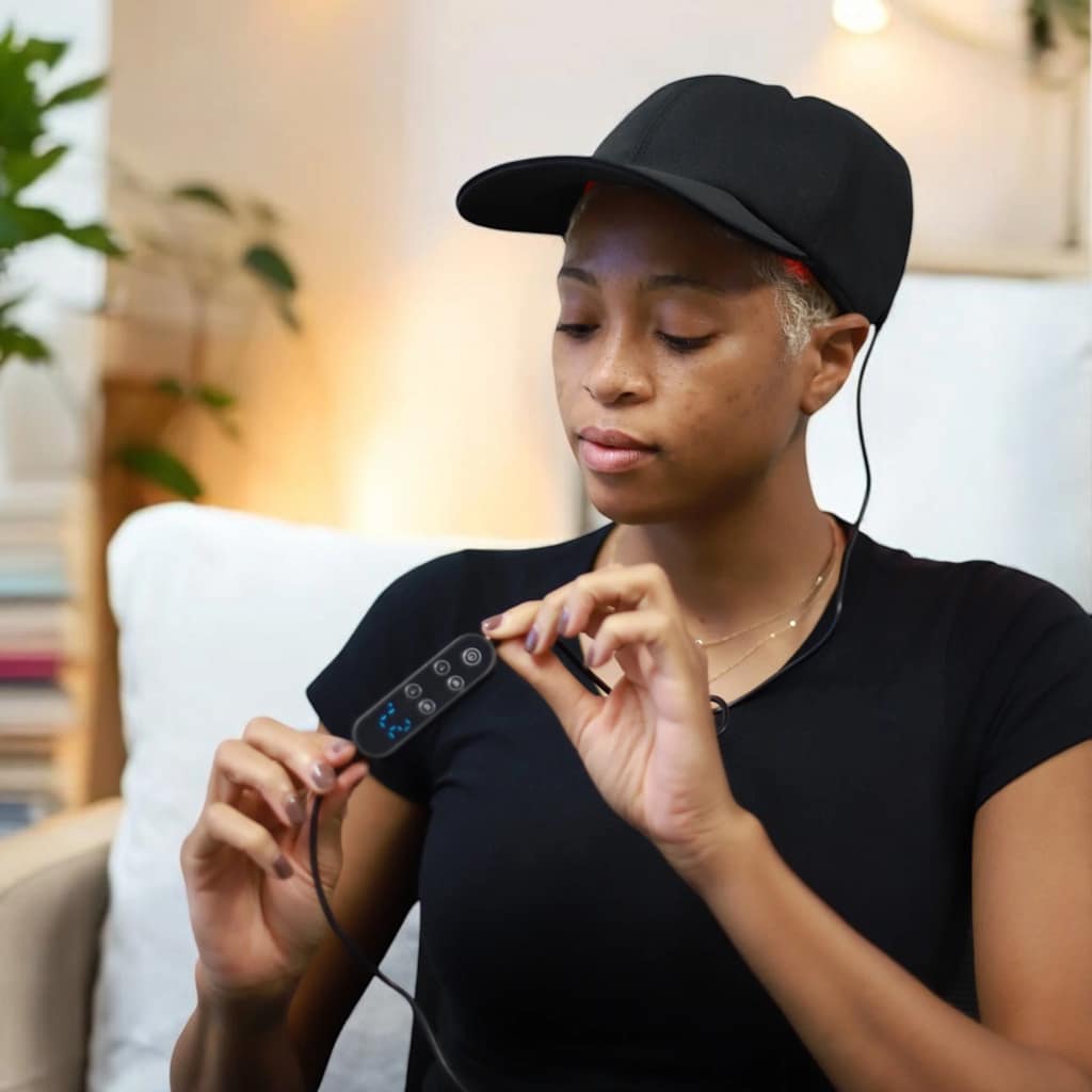 Woman adjusting Therasage Red Light Hat settings during portable battery-powered treatment session