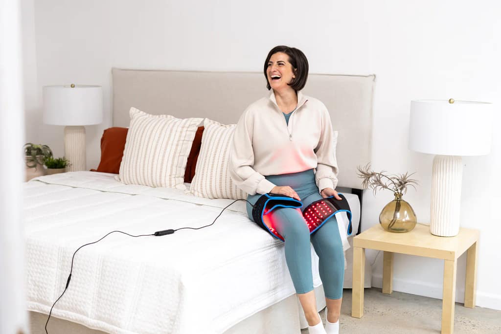 Woman relaxing with LifePro Red Light Belt wrapped around leg for evening pain relief routine