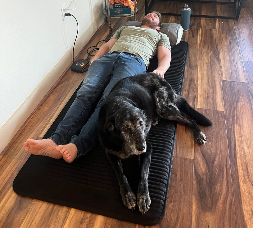 Man relaxing on Align Stealth PEMF Mat with dog, stress relief session