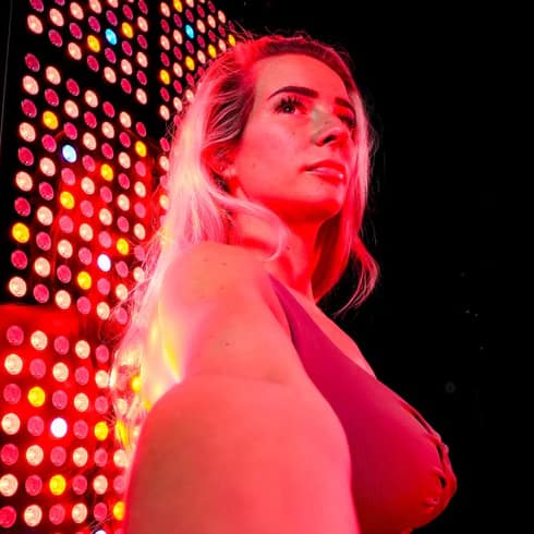 User next to high intensity red light therapy panel for recovery
