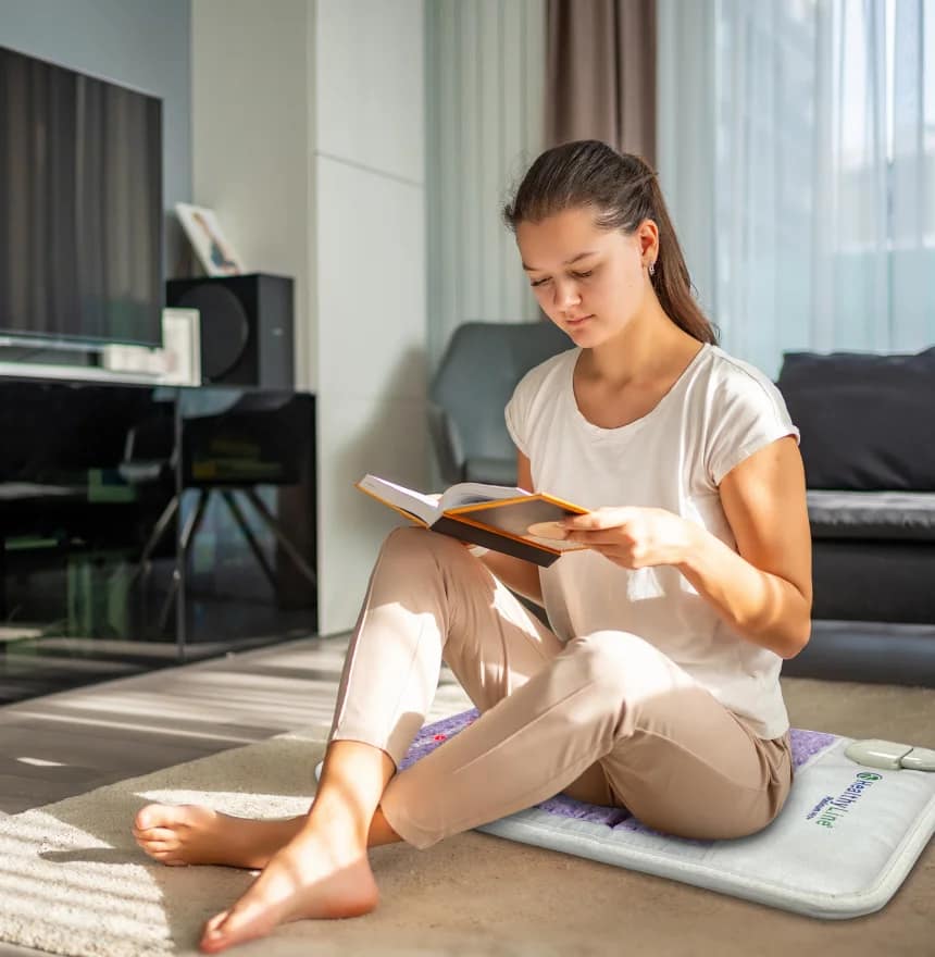 Woman relaxing and reading on HealthyLine Platinum PEMF MiniMat for premium therapy