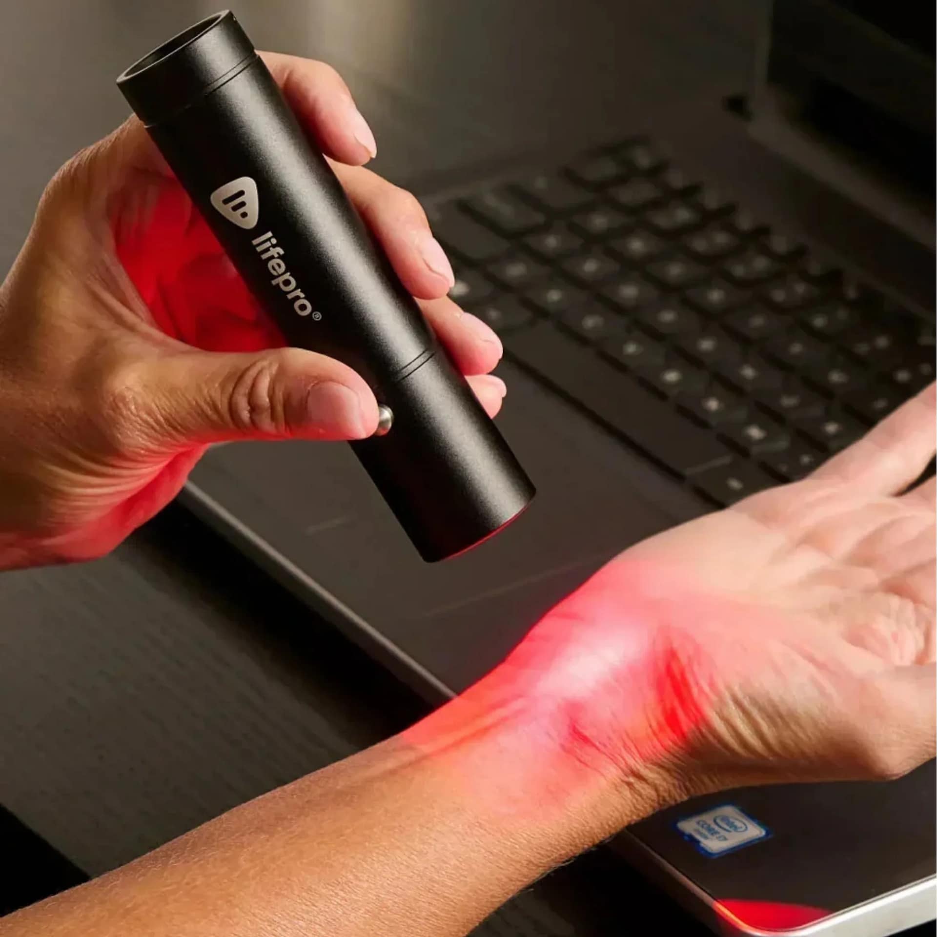 Person multitasking with LifePro Lumicure LED Torch on wrist during desk work for joint therapy