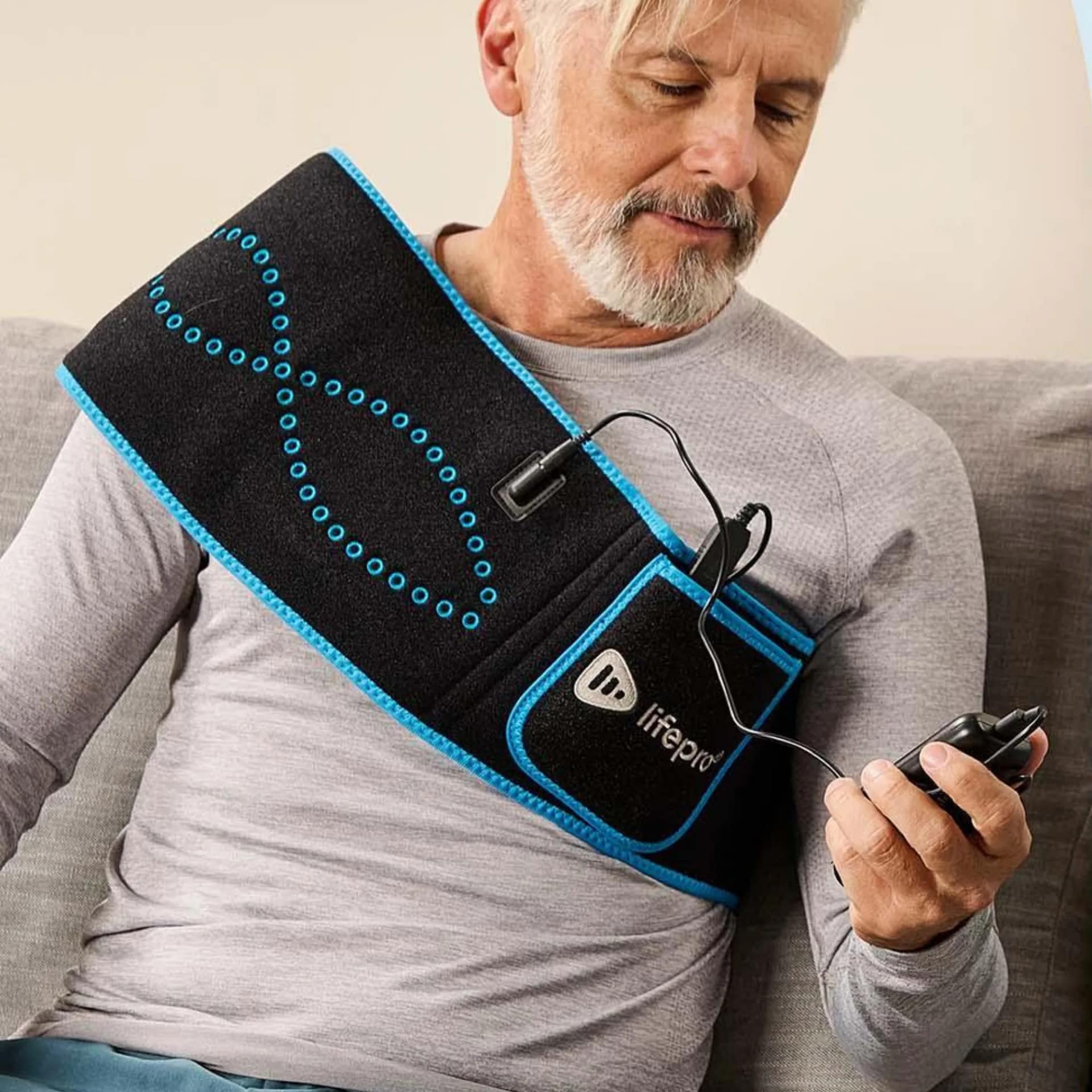 Man adjusting LifePro AllevaRed Belt settings while wearing on shoulders for upper body therapy